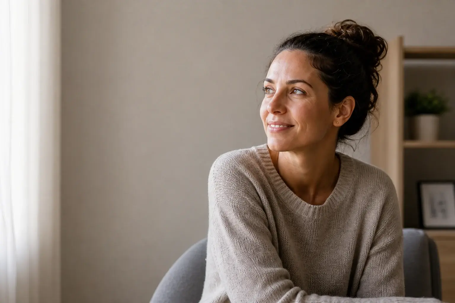 A woman seated in warm window light with a hopeful expression
